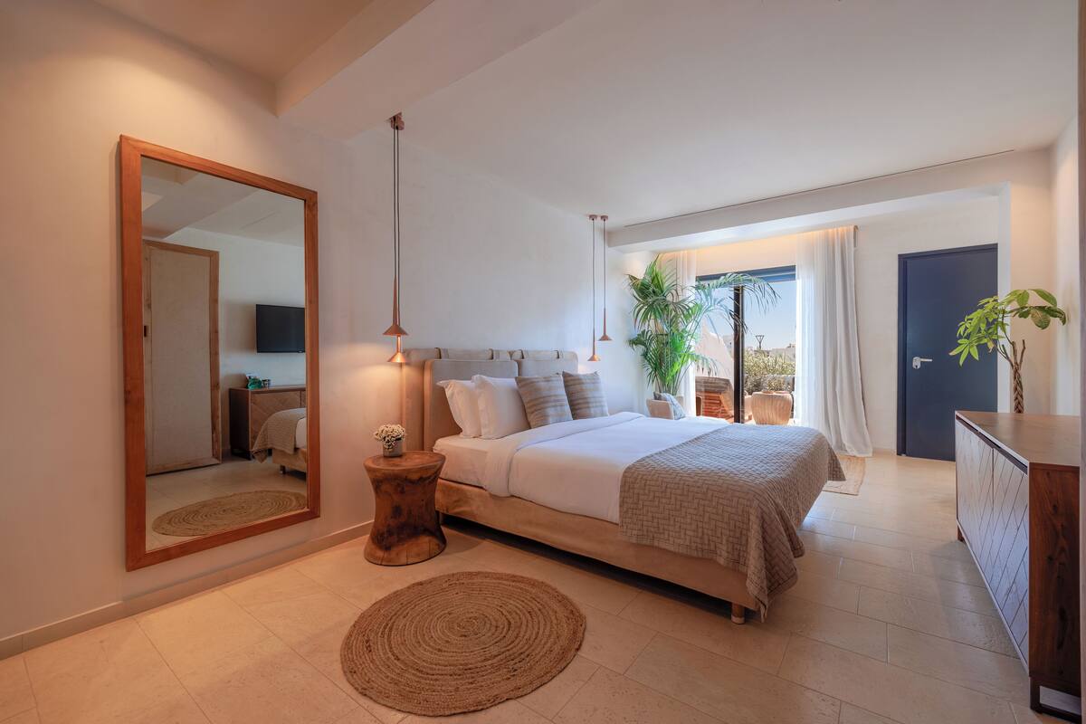 Un dormitorio moderno con una cama grande, mesitas de noche, un espejo y vistas al exterior.