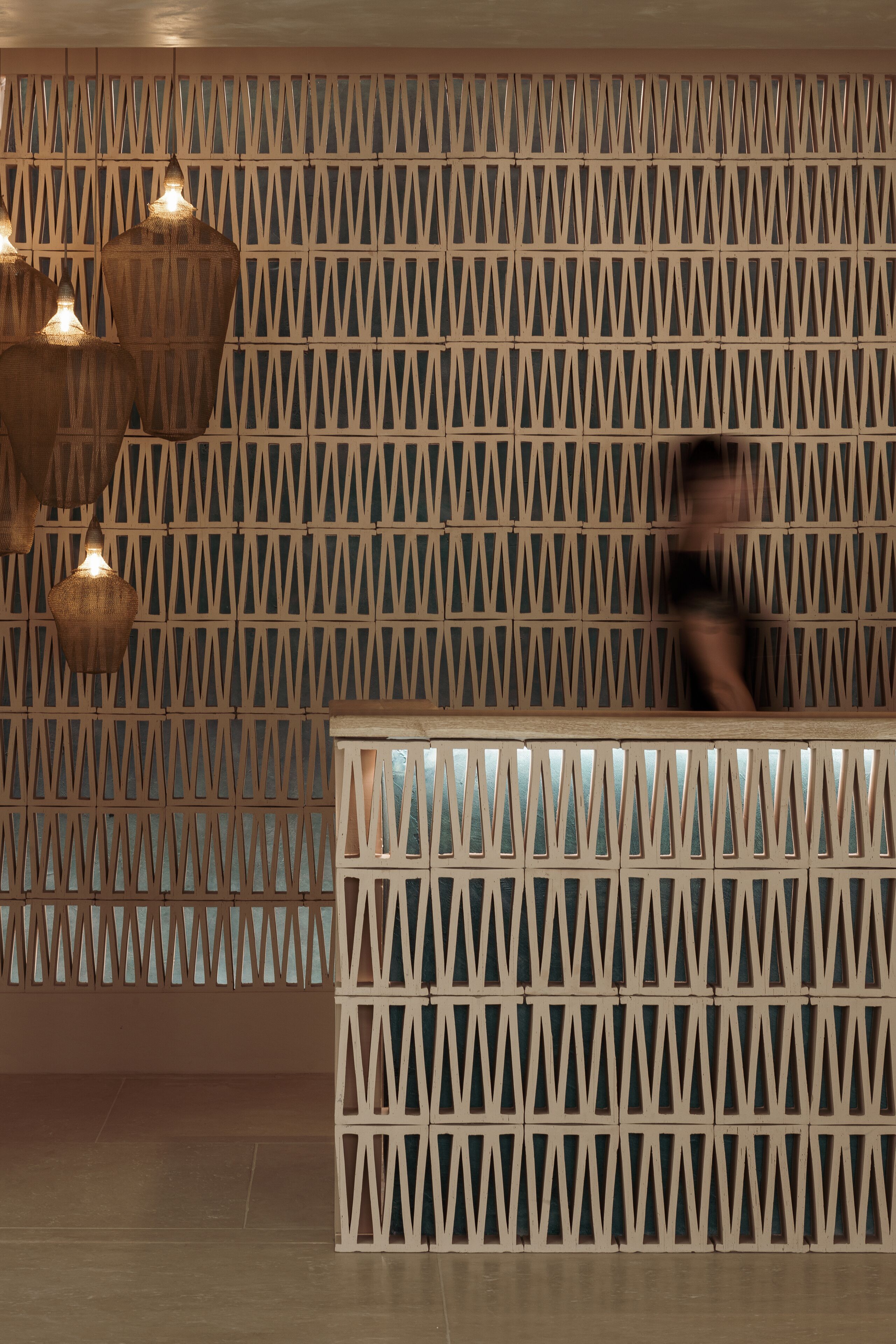 Un área de recepción con un muro de diseño geométrico y lámparas colgantes.