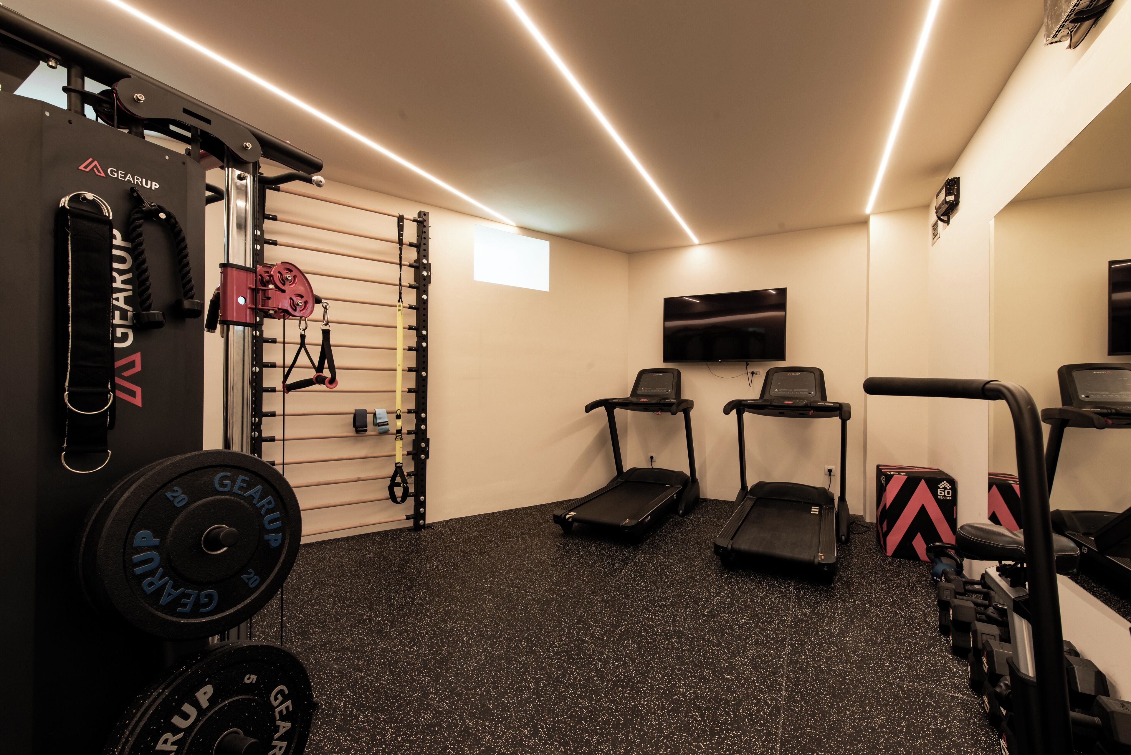 Un gimnasio con cintas de correr, equipo de levantamiento de pesas y un televisor en la pared.