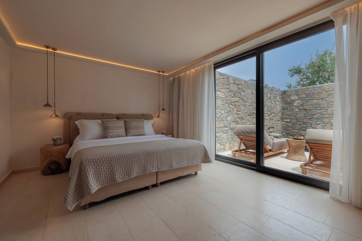 Un dormitorio con una cama grande, una mesita de noche y vistas a un área de estar exterior a través de una puerta corrediza de vidrio.