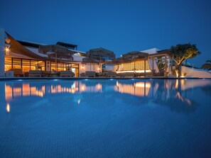 Zona junto a la piscina con sillones y sombrillas, reflejando la superficie del agua.