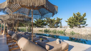 Zona piscina con poltrone prendisole, una piscina e un muro in pietra.