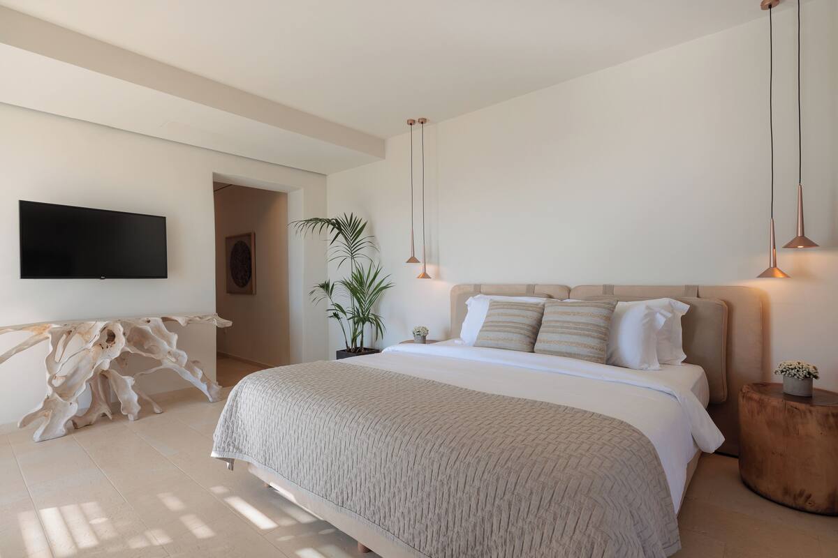 Un dormitorio moderno con una cama grande, un televisor de pantalla plana montado en la pared e iluminación colgante.