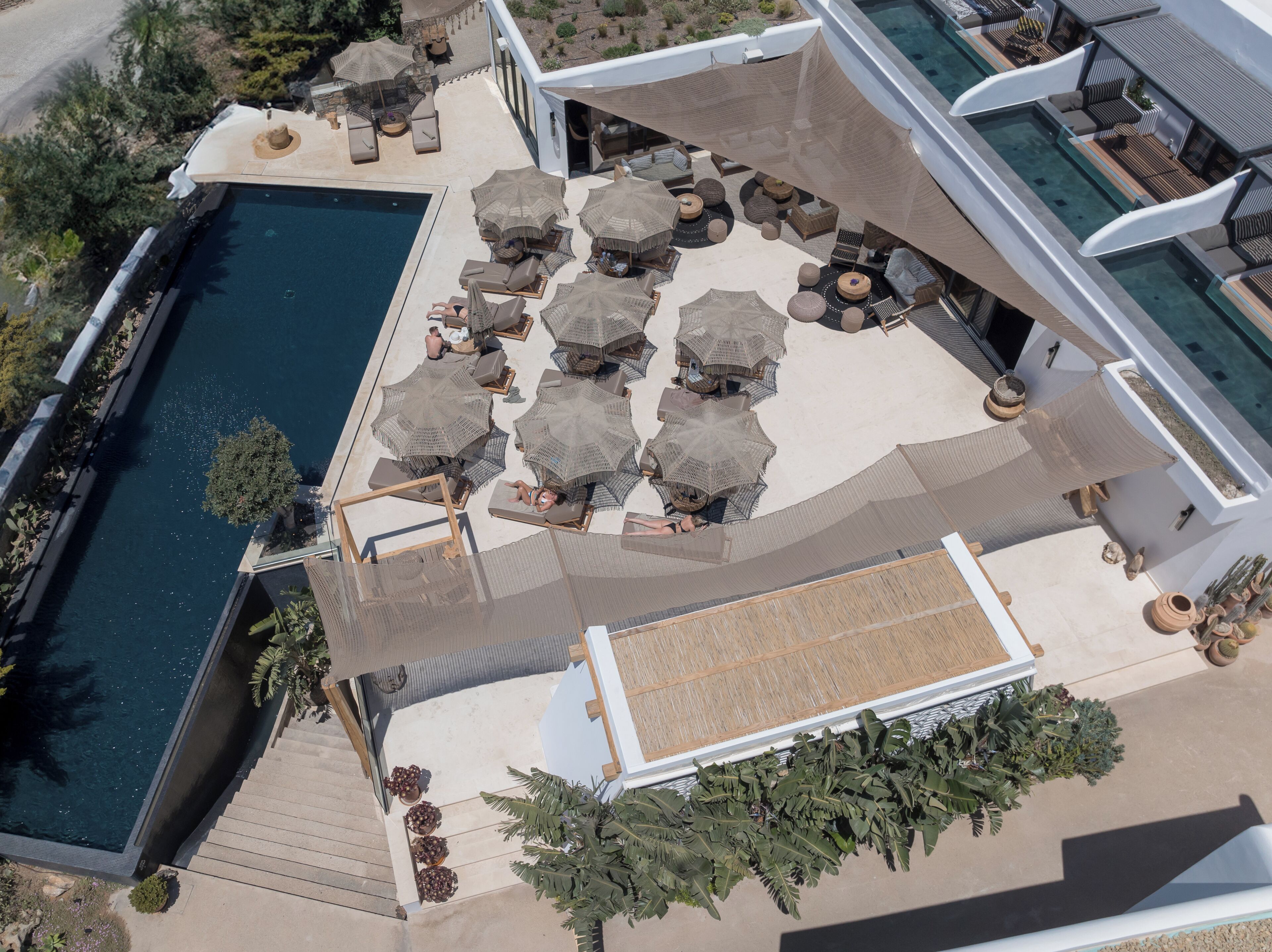 An aerial view of a resort with a swimming pool, sun loungers, and umbrellas.