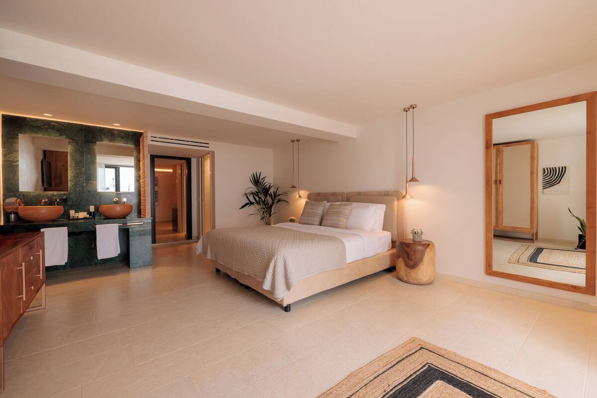 Un dormitorio moderno con una cama grande, dos mesitas de noche, un espejo y un tocador con dos lavamanos.