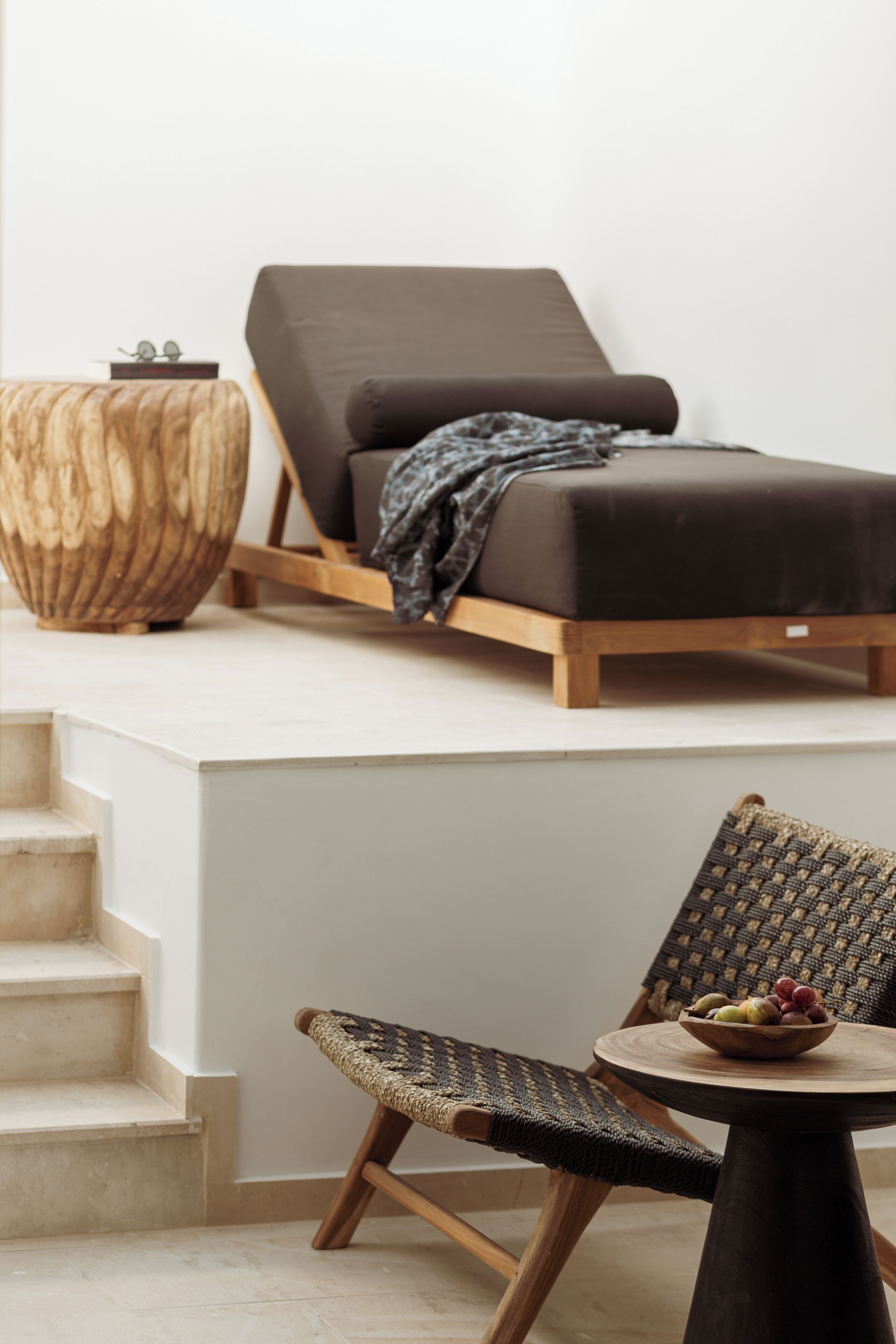 A modern room with a wooden bench, a small round table with a bowl of fruit, and a lounge chair with a blanket.