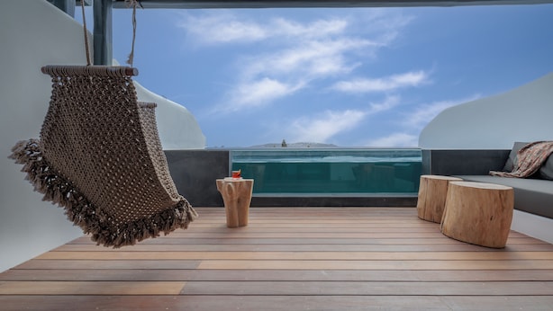 Un pontile in legno con un oggetto tessuto appeso, due sgabelli di legno e un'area salotto con cuscini.