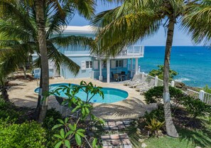 A beachfront property with a pool, lounge chairs, and a view of the ocean.