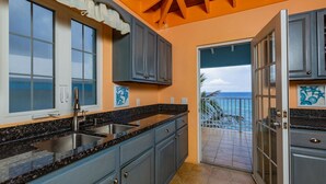 A kitchen with granite countertops, grey cabinets, and a view of the ocean through a sliding glass door. - Cliffside at Cane Bay - 3 bed/ 4 bath seaside home with private pool. (Cane Bay beach)
