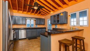 A kitchen with a central island, bar stools, and a ceiling fan. - Cliffside at Cane Bay - 3 bed/ 4 bath seaside home with private pool. (Cane Bay beach)