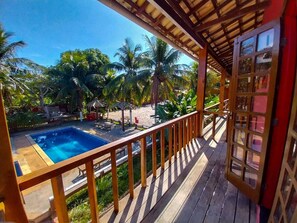 Um deck de madeira com piscina, cercado por palmeiras e um céu claro.