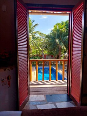 Vista desde una habitación con piso de madera que da a un área de piscina con muelle de madera y palmeras.