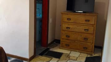 A room with a wooden dresser, a television on top, and a tiled floor.