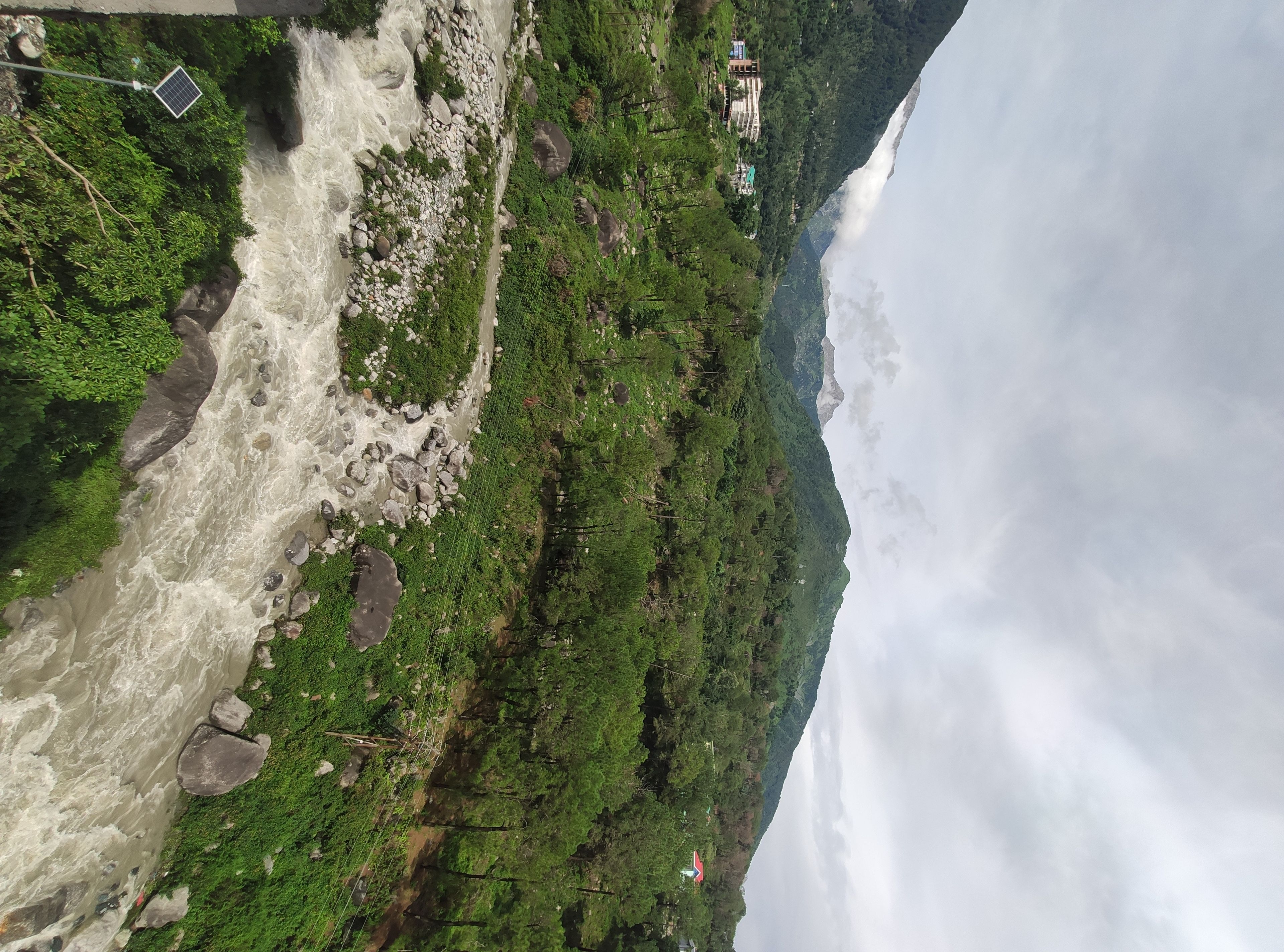 A river flowing through a mountainous area with greenery and a few buildings in the distance.