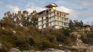 A multi-story building with a flat roof and a balcony, surrounded by rocky terrain and a stream. - Manuni Inn - Riverside Hotel (Dharamshala)