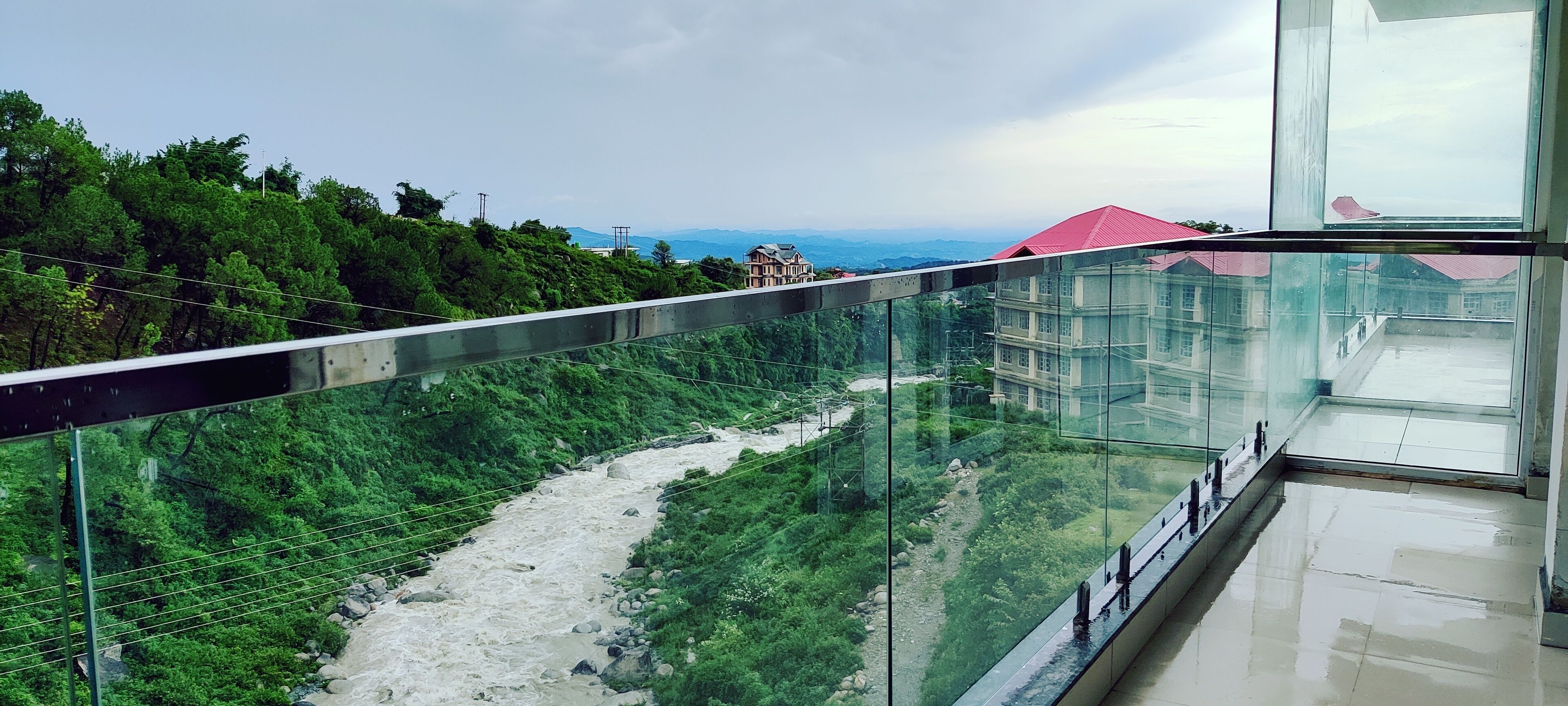 Een glazen balkon met uitzicht op een rivier, met een gebouw met rode daken op de achtergrond.