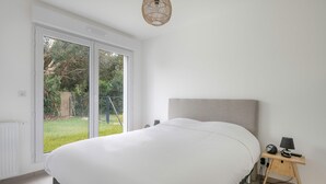 Un dormitorio con una cama grande, una mesita de noche con lámpara y vistas a un jardín a través de un ventanal corredero.