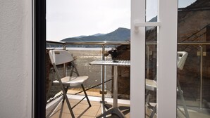Un balcón con mesa y sillas, con vista a un cuerpo de agua y montañas.