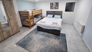 Un dormitorio con una cama litera, una cama individual, un cuadro en la pared y una puerta con ventanal.