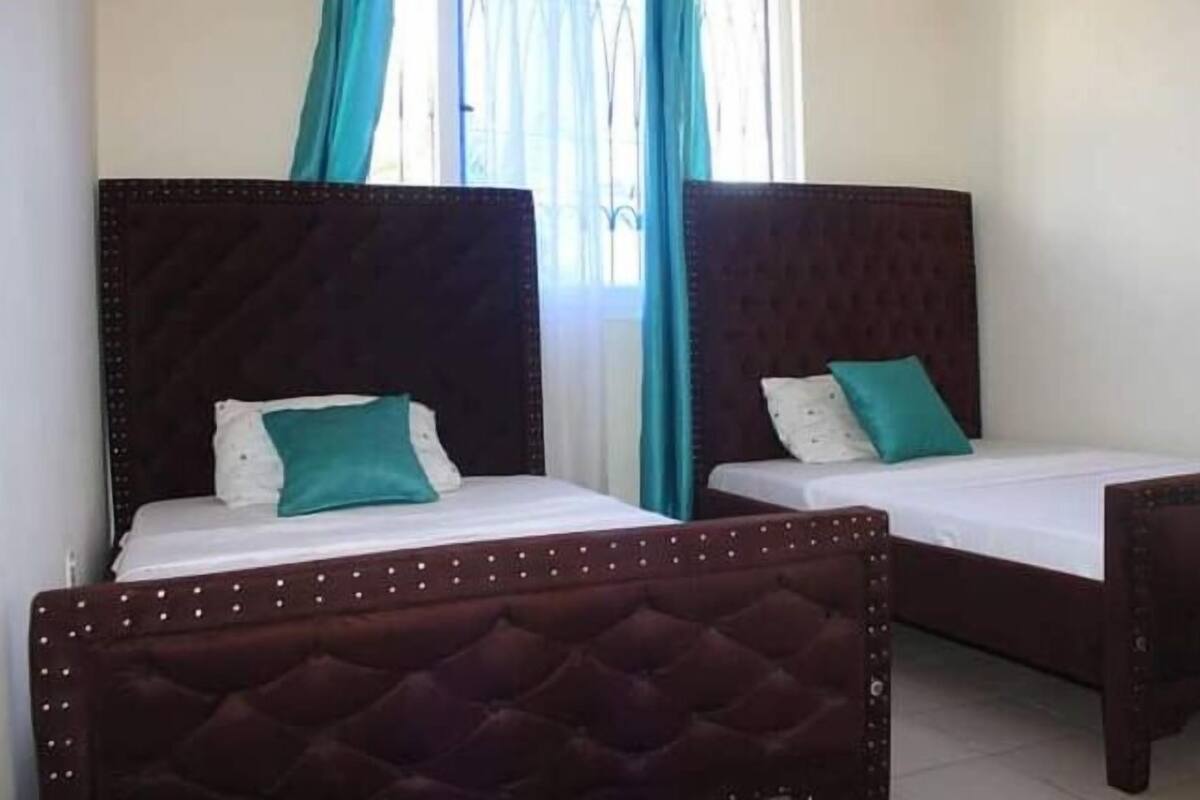 Two beds with dark headboards, white bedding, and teal pillows.