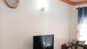 A living room with a TV on a wooden stand, a dining table with chairs, a sofa, and a patterned rug. - Stay.Plus Mtwapa Luxe Apartments (Mtwapa)