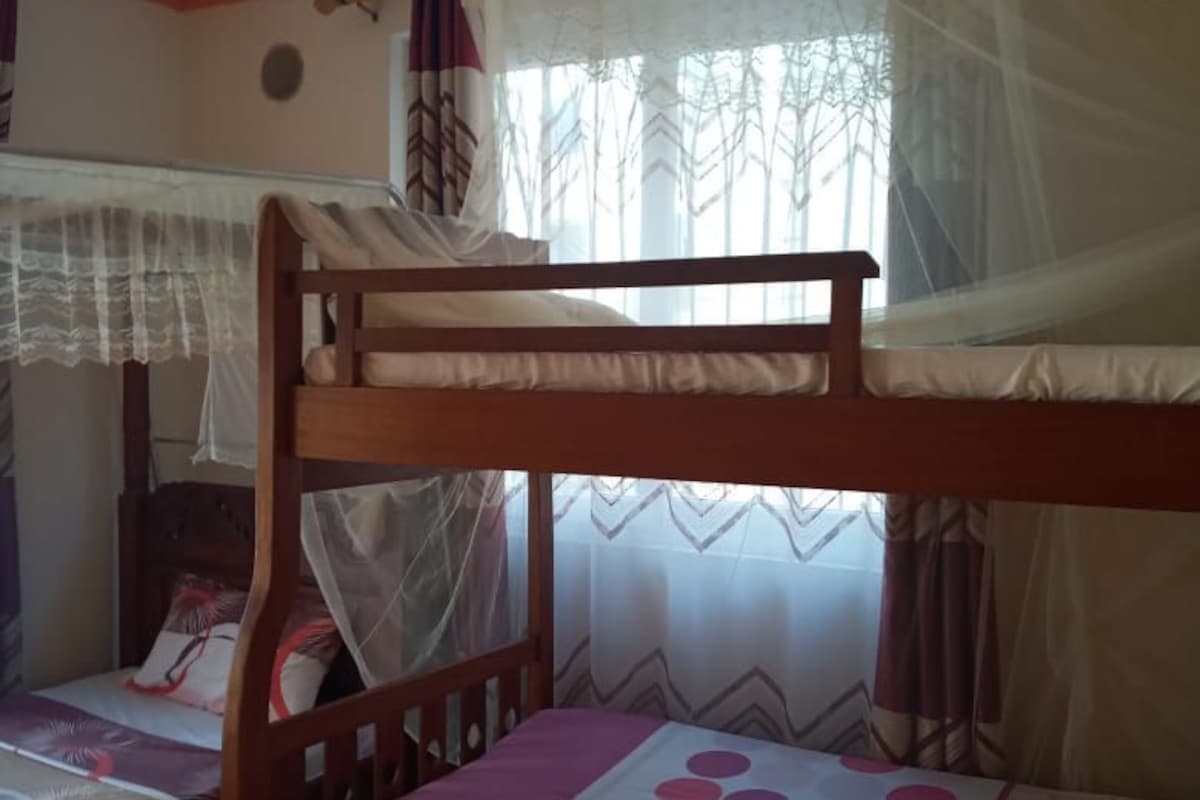 A room with a bunk bed, a single bed, and a mosquito net over the window.