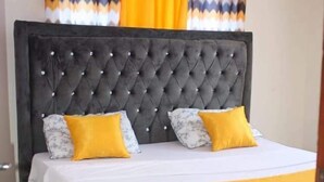A bed with a tufted headboard, two pillows, and a yellow bedspread. - Stay.Plus Mtwapa Luxe Apartments (Mtwapa)