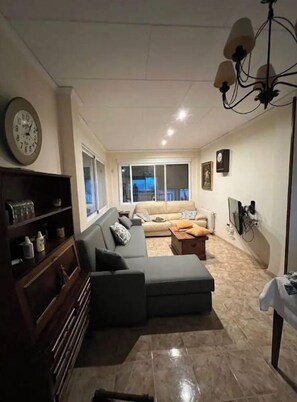 A living room with a sofa, a wooden cabinet, a chandelier, and a large window.