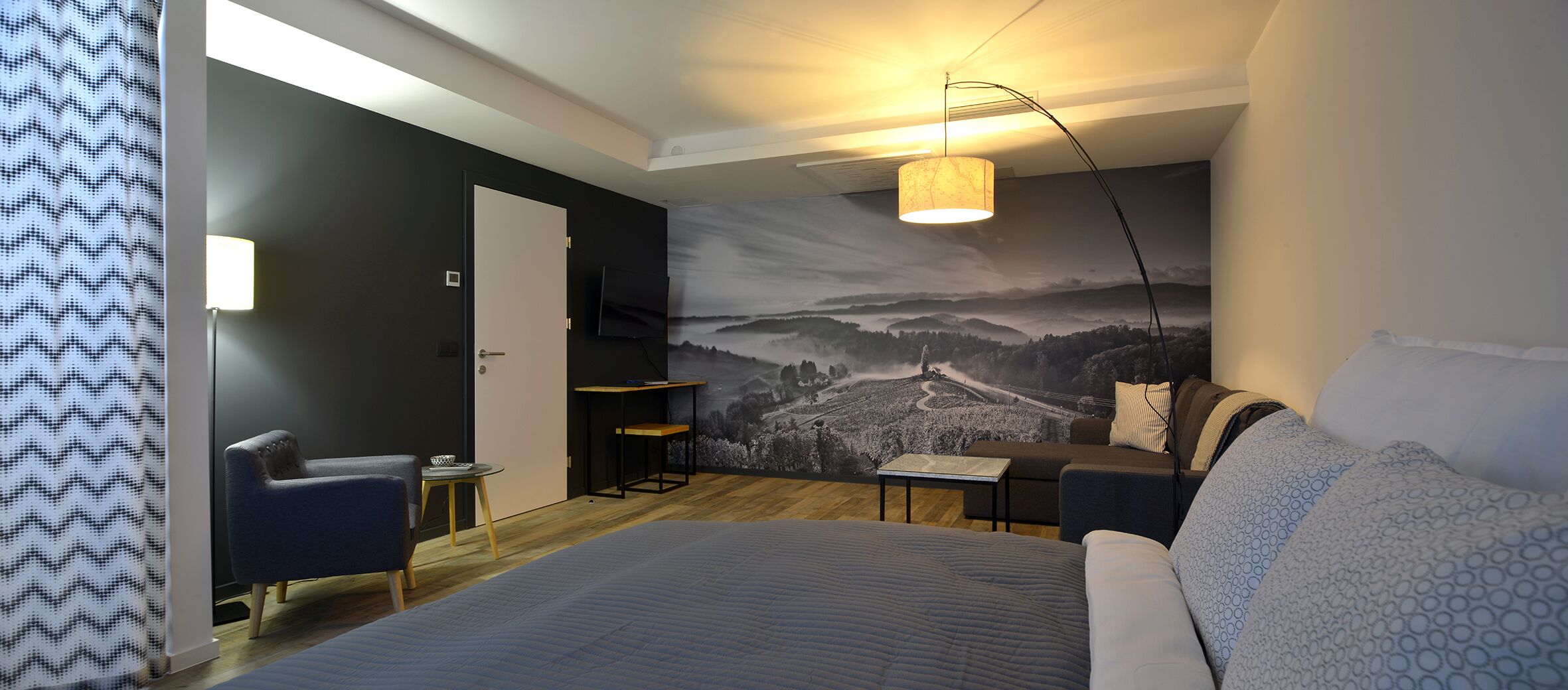A modern bedroom with a large bed, a desk, a chair, and a mural of a mountainous landscape.