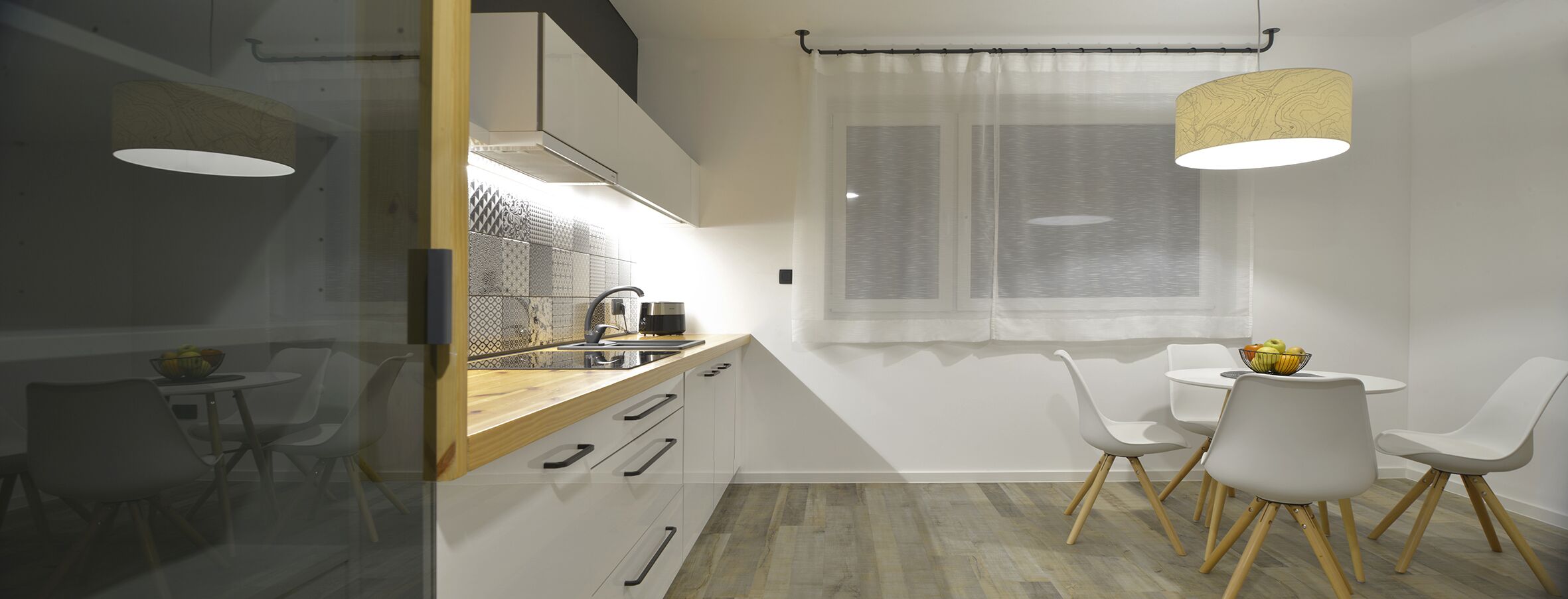A modern kitchen with a wooden countertop, white cabinets, and a dining area with white chairs and a small table.