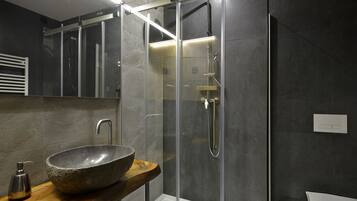 A modern bathroom with a glass-enclosed shower, a stone basin, and a wooden shelf.
