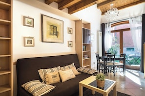 A cozy living room with a sofa, a coffee table, and a dining area with chairs and a table. There are framed pictures on the wall and a window with curtains. - Duplex: spacious apartment with terrace and air conditioning at the entrance of Venice. (Venezia)