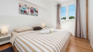 A bedroom with a large bed, a nightstand, a painting, and a window with curtains.