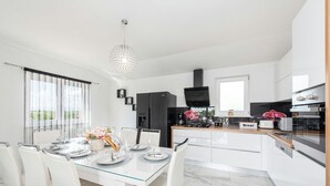 A modern kitchen with white cabinetry, a black refrigerator, a built-in oven, and a coffee machine.