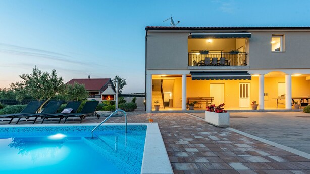 A two-story house with a swimming pool, outdoor seating, and a well-lit patio area.