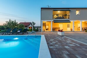 A two-story house with a swimming pool, outdoor seating, and a well-lit patio area. - Villa Silentium, rural area, heated pool, volleyball court, children's playground (Benkovac)