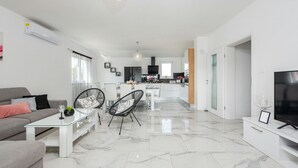 A modern living room with a glass coffee table, a grey sofa, and a dining area with chairs and a table.