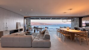 A modern living room with a large sofa, dining area, and a view of the sea. - Untold Mykonos (Mykonos)