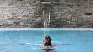 Eine Person schwimmt in einem Pool, im Hintergrund eine Steinmauer.