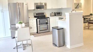 A modern kitchen with white cabinets, stainless steel appliances, and a small dining area with a table and chairs. - ★ Beautiful 3 Bedroom Home - Parking, Wi-fi, near Hwy 401, 6 Beds available (Cambridge)