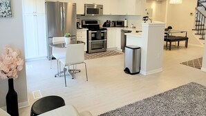 A modern kitchen with white cabinets, stainless steel appliances, a dining area with a white table and chairs, and a staircase leading to another level. - ★ Beautiful 3 Bedroom Home - Parking, Wi-fi, near Hwy 401, 6 Beds available (Cambridge)