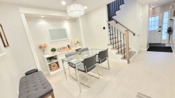 A modern dining area with a glass table and chairs, a chandelier, and a staircase leading to a door. - ★ Beautiful 3 Bedroom Home - Parking, Wi-fi, near Hwy 401, 6 Beds available (Cambridge)