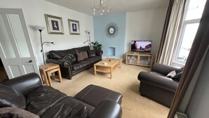 Ein Wohnzimmer mit einer schwarzen Ledersofa, einem Holztisch, einem Fernseher auf einem Holzboden und einem Bücherregal.