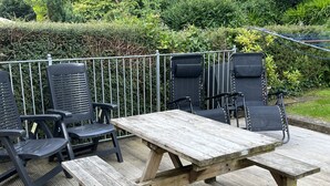 Eine Holzterrasse mit Picknicktisch und schwarzen Stühlen.