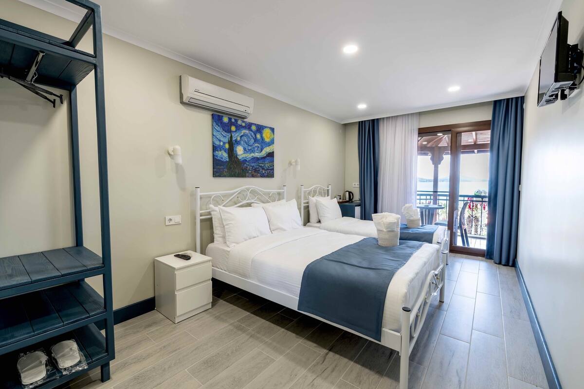 A bedroom with a bed, a nightstand, a shelf, a painting, and a balcony with curtains.