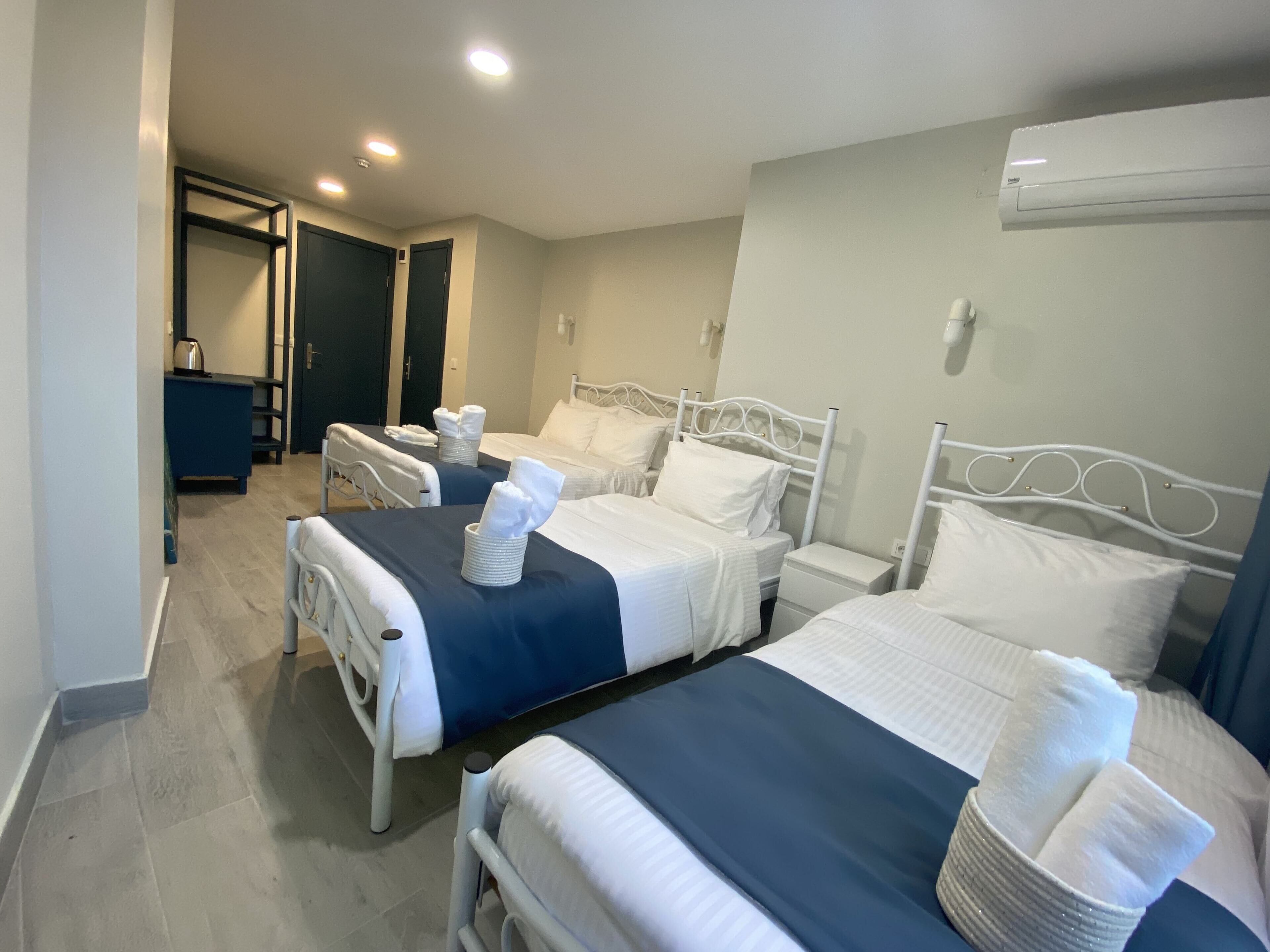 A hotel room with two beds, each with white linens and towels, a small bedside table, and a wall-mounted air conditioner.
