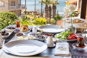 A table set for breakfast with various dishes, a vase with flowers, and a view of the sea and buildings. - Cunda Villa Anka (Ayvalik)