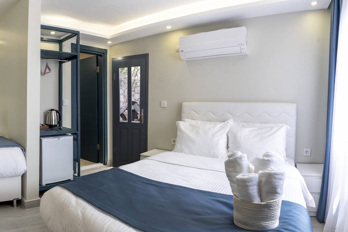 A hotel room with a bed, a desk, a chair, a small kitchenette, and a bathroom.