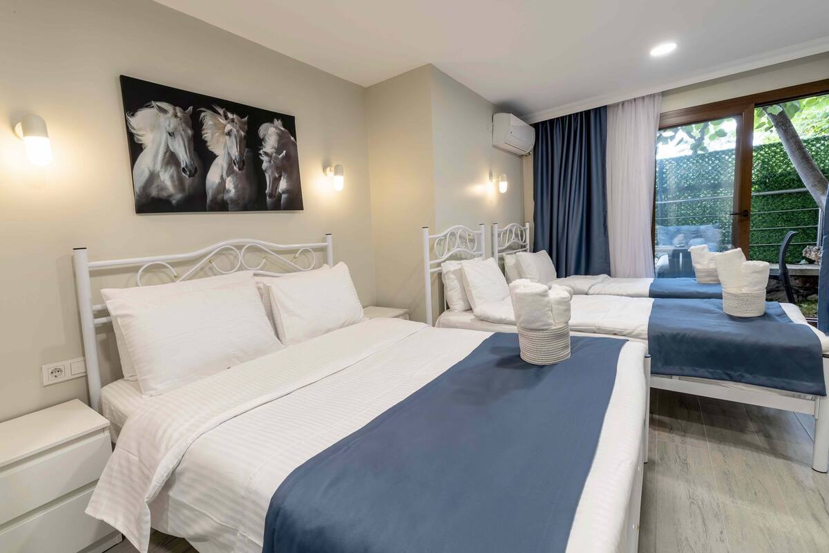 A hotel room with two beds, a large painting of horses, and a view of greenery outside.