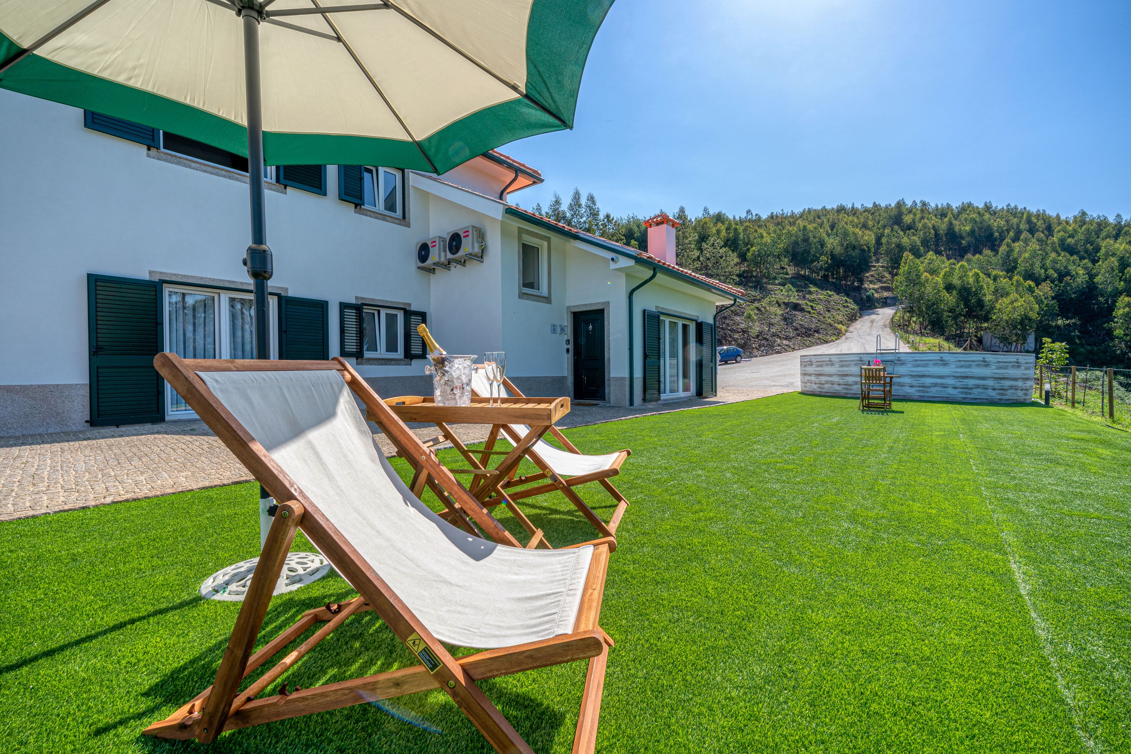 Ein zweistöckiges Haus mit gepflegtem Rasen, Außenmöbeln und Blick auf einen bewaldeten Hügel.